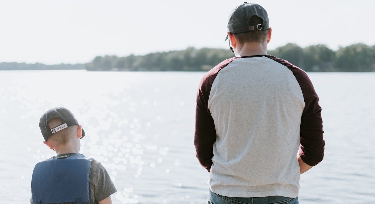 father and son standing at the edge of a lake fishing