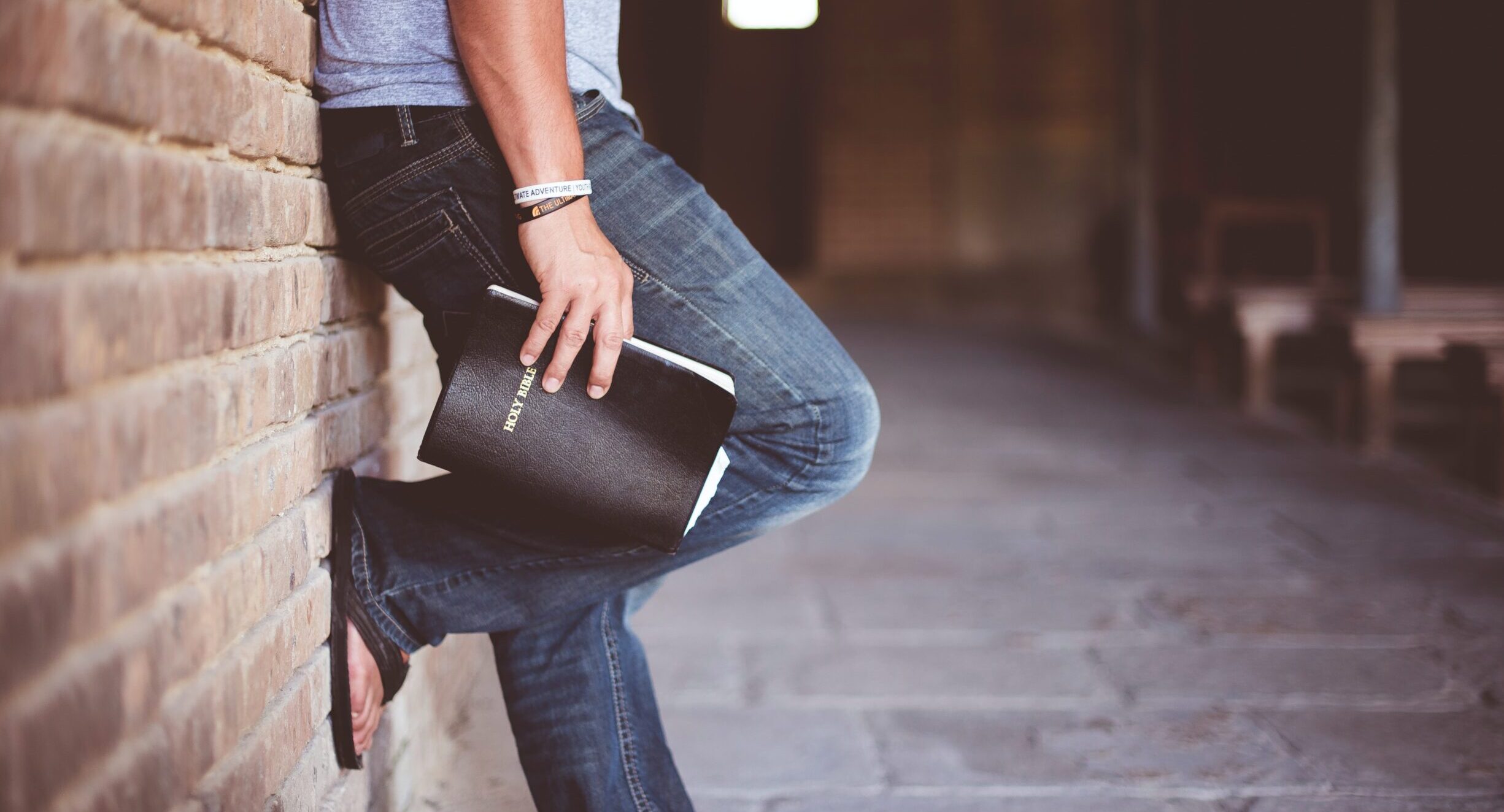 Man leaning against brick wall while holding a Bible