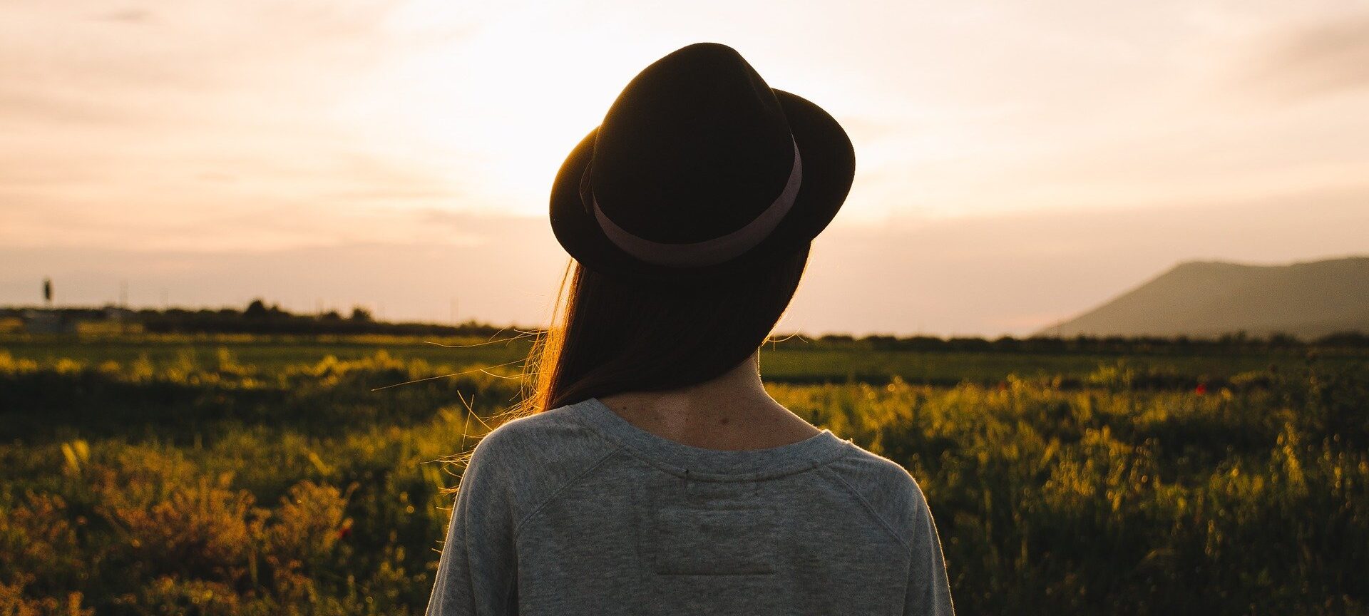 woman wearing hat standing in a field at sunset