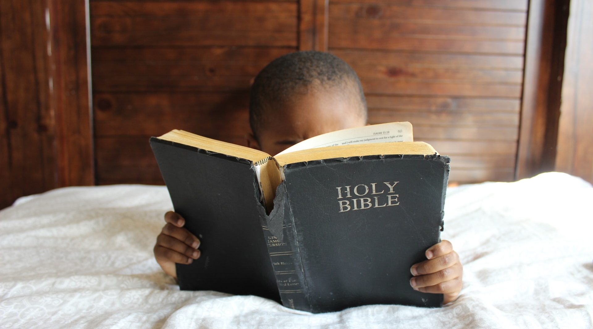 Little boy reading the Bible on a bed